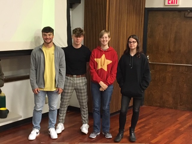 Four students stand in a room