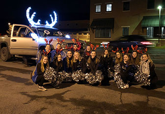 cheerleaders kneel in front of truck with lighted antlers