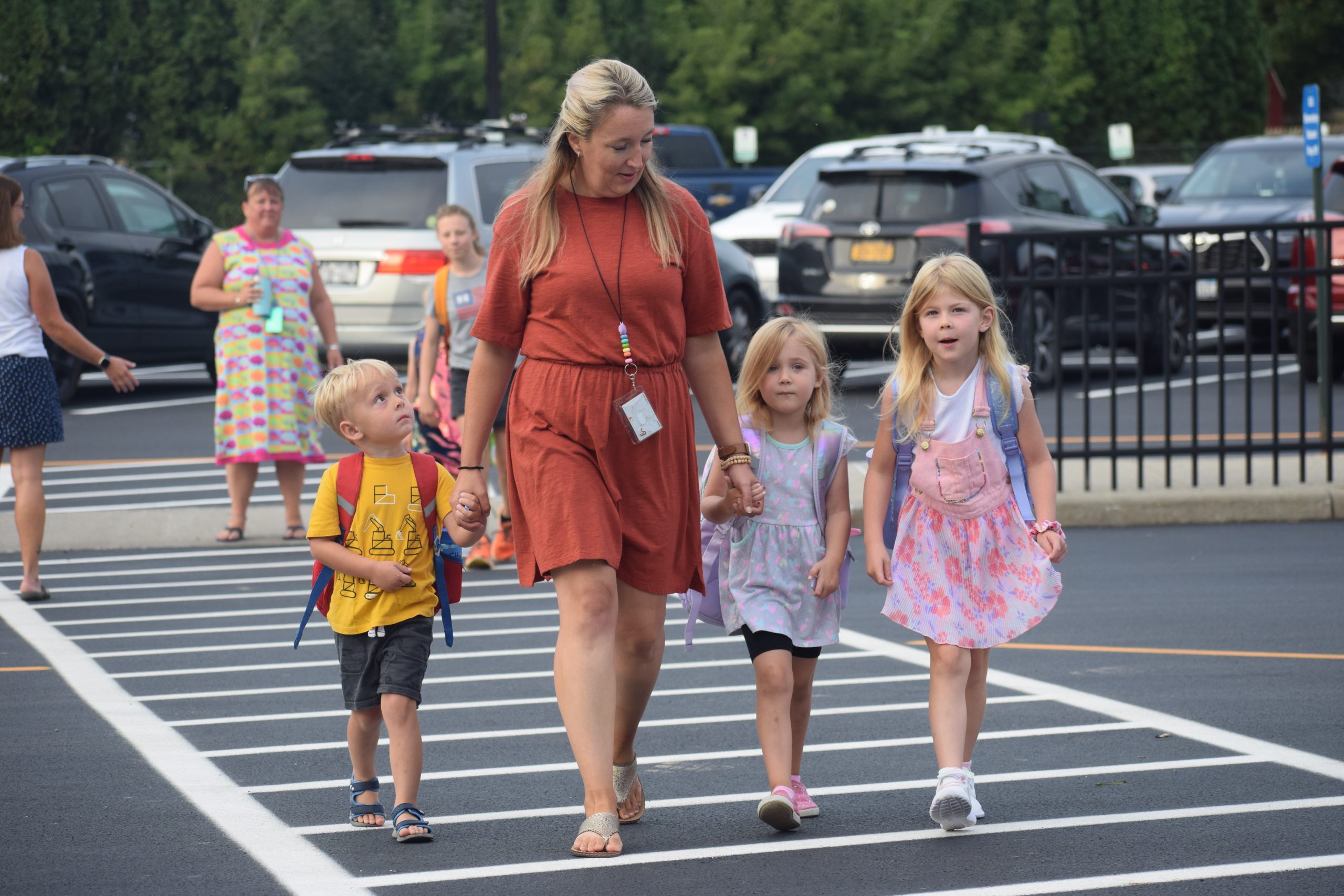 A staff member helps students cross a parking lot