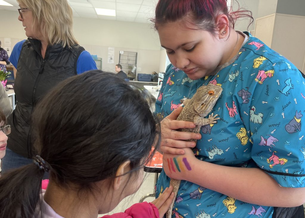 An older student holds a lizard for a younger student