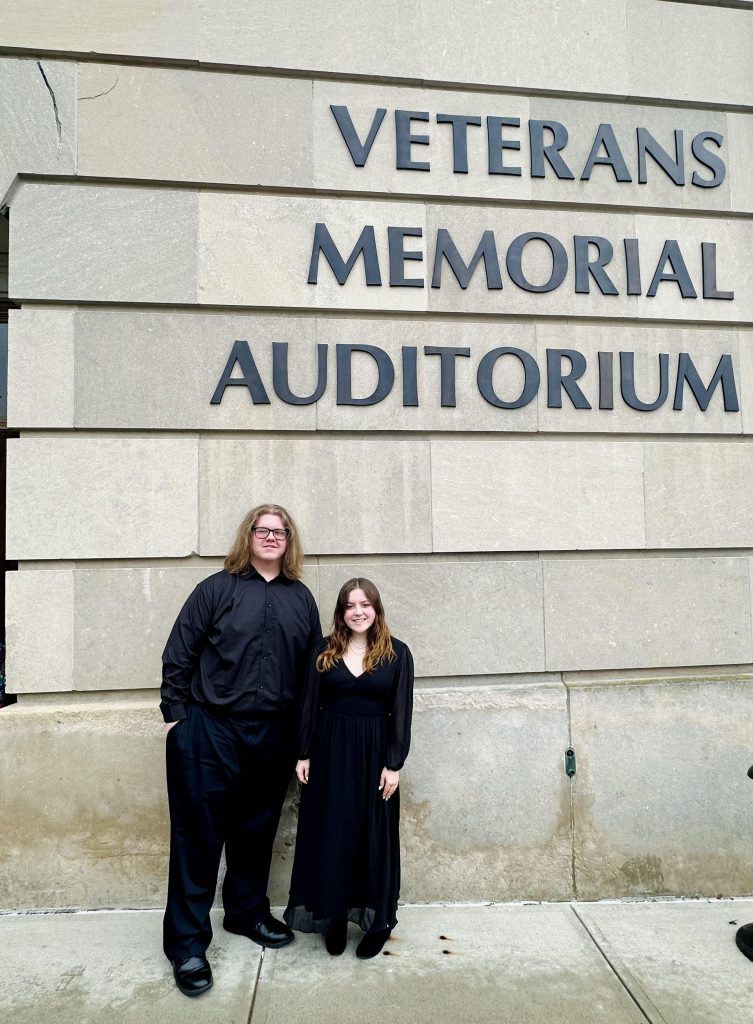 Two students stand next to a wall