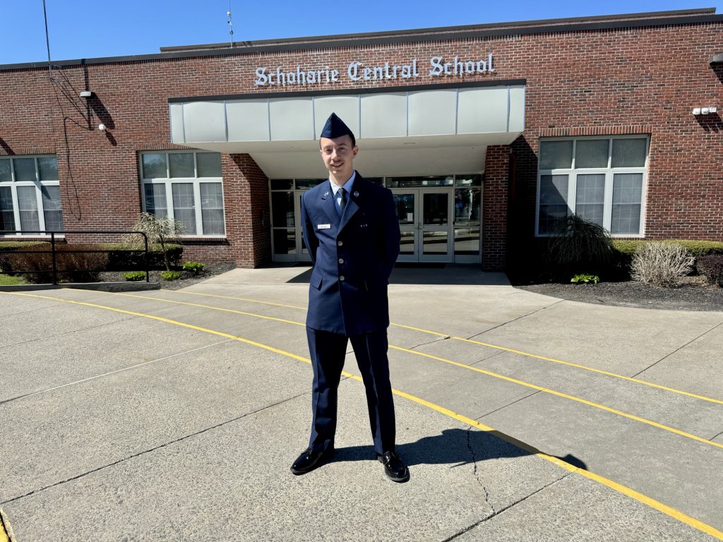 An airman stands in front of a school
