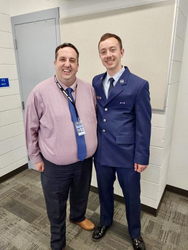 An airman stands next to a principal