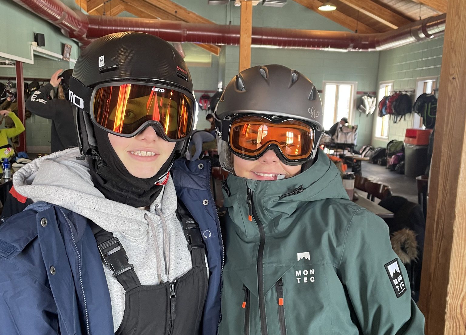 Two adventure Club students pose in a ski lodge wearing ski clothing, helmets and goggles.