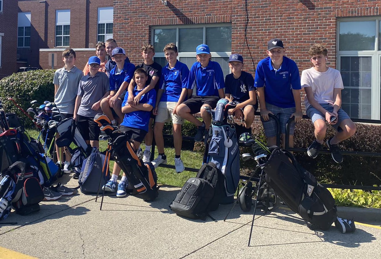 The boys golf team poses together outside surrounded by their golf bags.