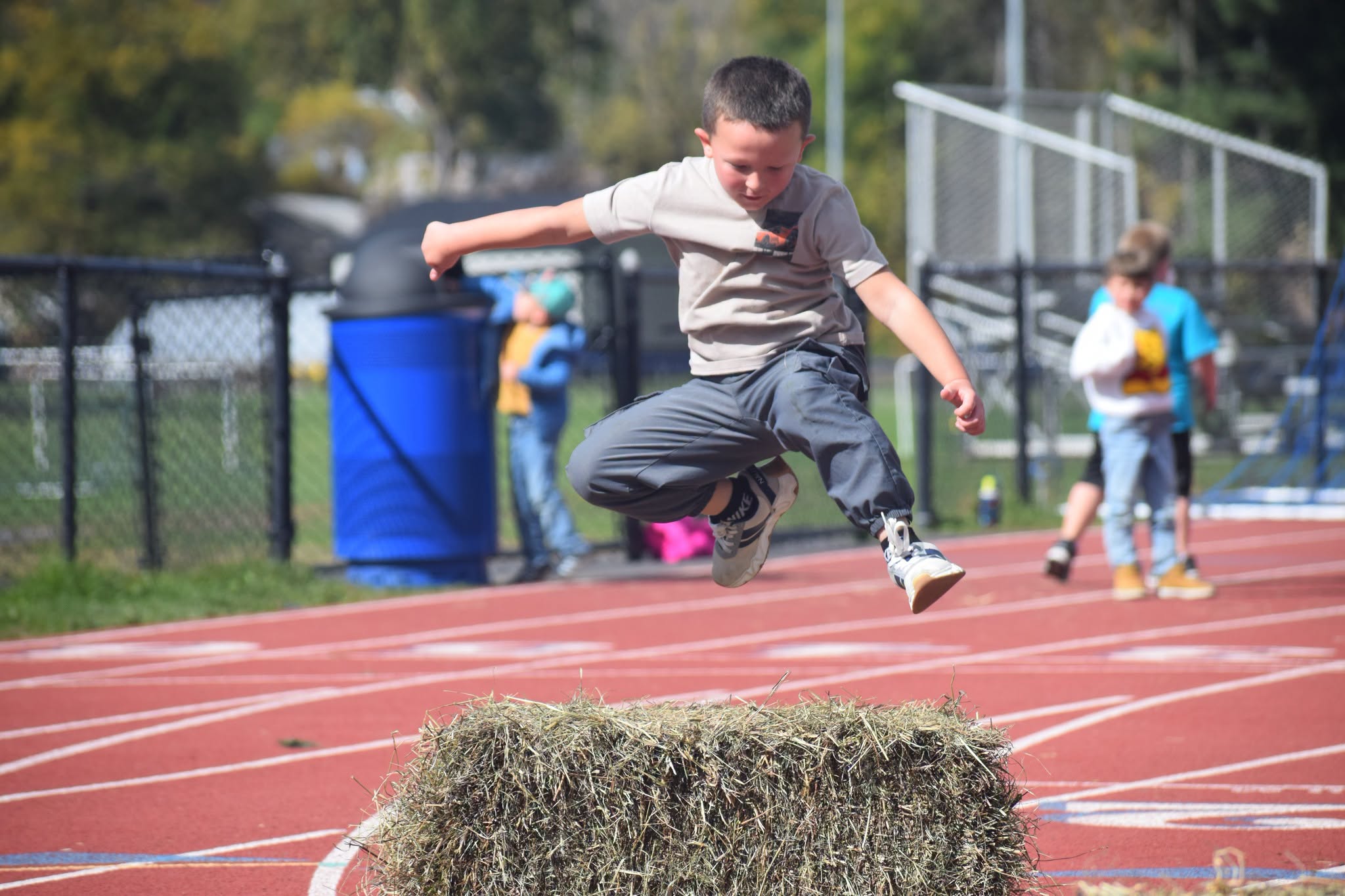 A kid jumps over a hay bale