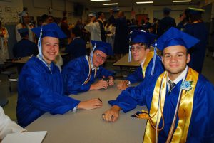 four male graduates sit at a table wearing their caps and gowns