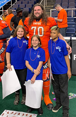 3 students pose with football player on field