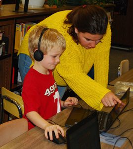 high school student assists elementary student at computer