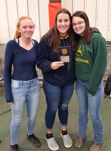 3 girls standing, one holds award plaque