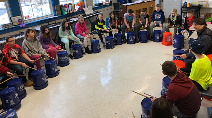seated students drum with their hands on buckets