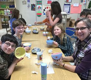 students and teacher at tables painting bowls