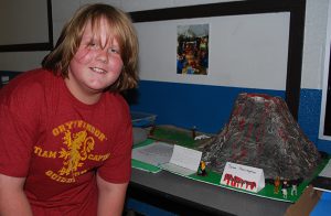 student poses next to his model volcano