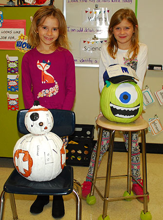 2 girls stand behind pumpkins