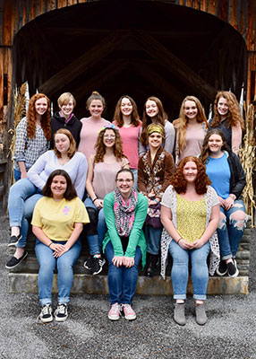 group of female students stand and sit at entrance of covered bridge